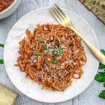 Overhead shot of Linguine Bolognese on a white plated topped with fresh parsley and a gold fork.