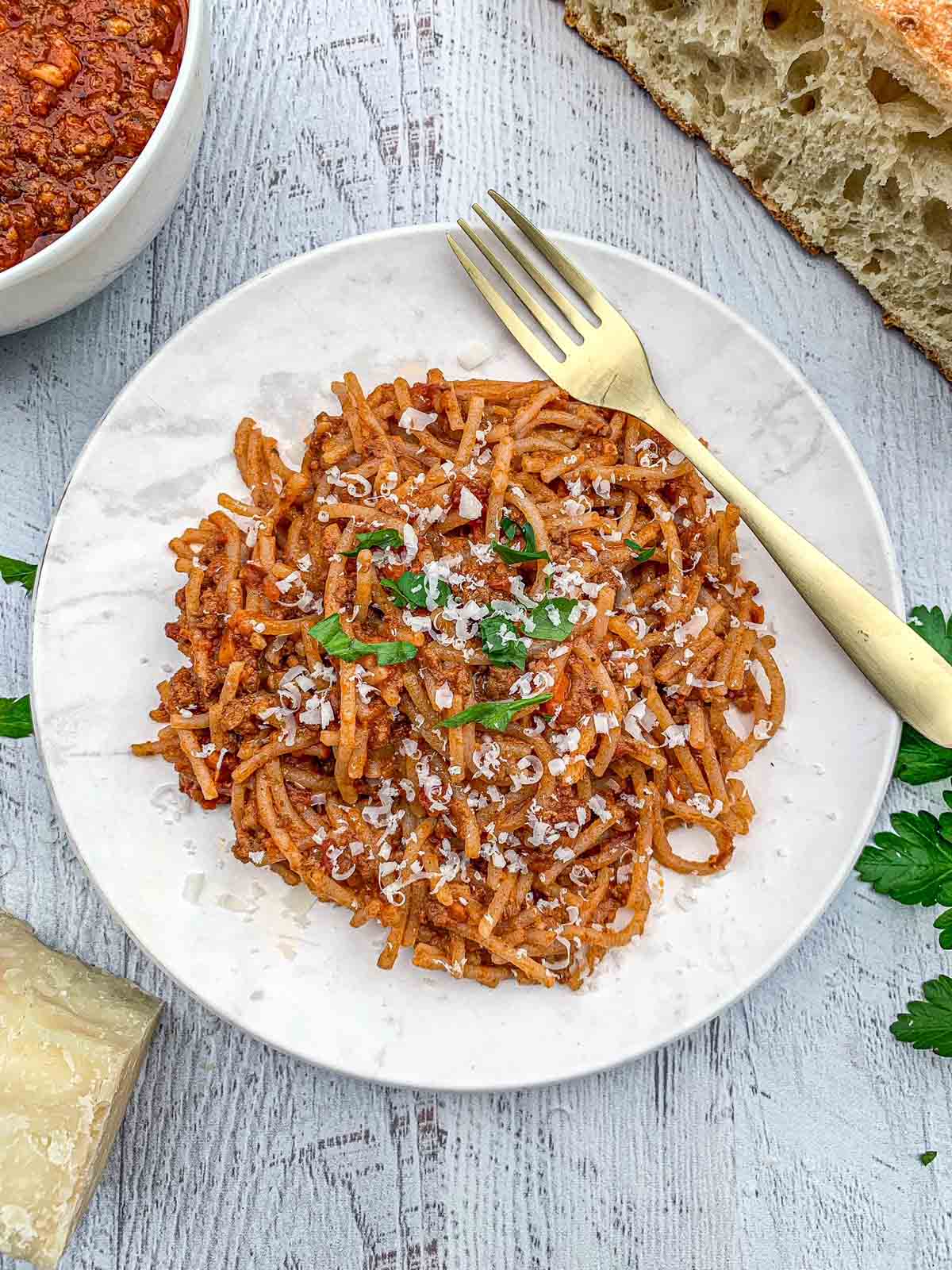 Overhead shot of Linguine Bolognese on a white plated topped with fresh parsley and a gold fork.