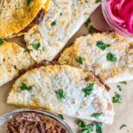 Barbacoa Quesadillas on parchment paper with pickled red onions next to them.