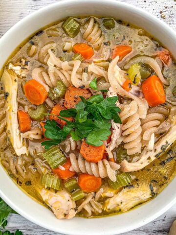 Dutch Oven Chicken Noodle Soup in a white bowl with parsley, cheese and pepper.