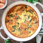 High Protein egg Bake in a white baking dish with spinach and a green napkin.