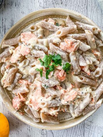 Pasta Alla Salmone in a serving plate with lemon and thyme next to it.