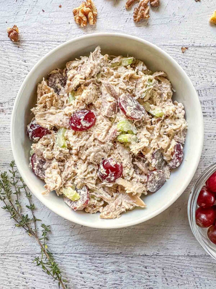 California Chicken Salad in a white bowl. A sprig of thyme and red grapes are next to the bowl.