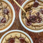Three servings of chocolate chip cookie dough baked oats in white ramekins with a gold spoon in one.