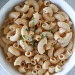 Cottage cheese mac and cheese in a white bowl topped with parsley and extra cheddar cheese.