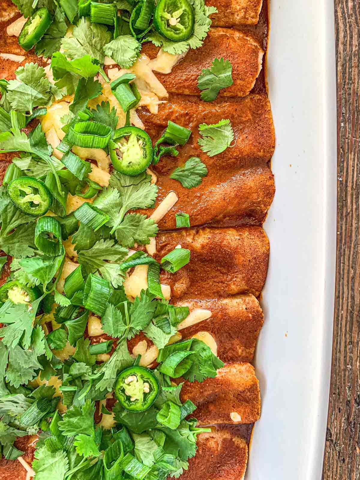 Gluten-Free chicken enchiladas topped with red sauce, japalenos, cilantro and white cheddar cheese.