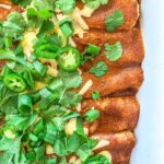 Gluten-Free chicken enchiladas topped with red sauce, japalenos, cilantro and white cheddar cheese.