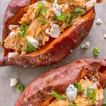 Slow cooker buffalo chicken stuffed sweet potatoes topped with blue cheese and green onion.