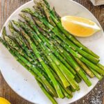 Smoked asparagus on a white plate topped with sea salt and lemon.