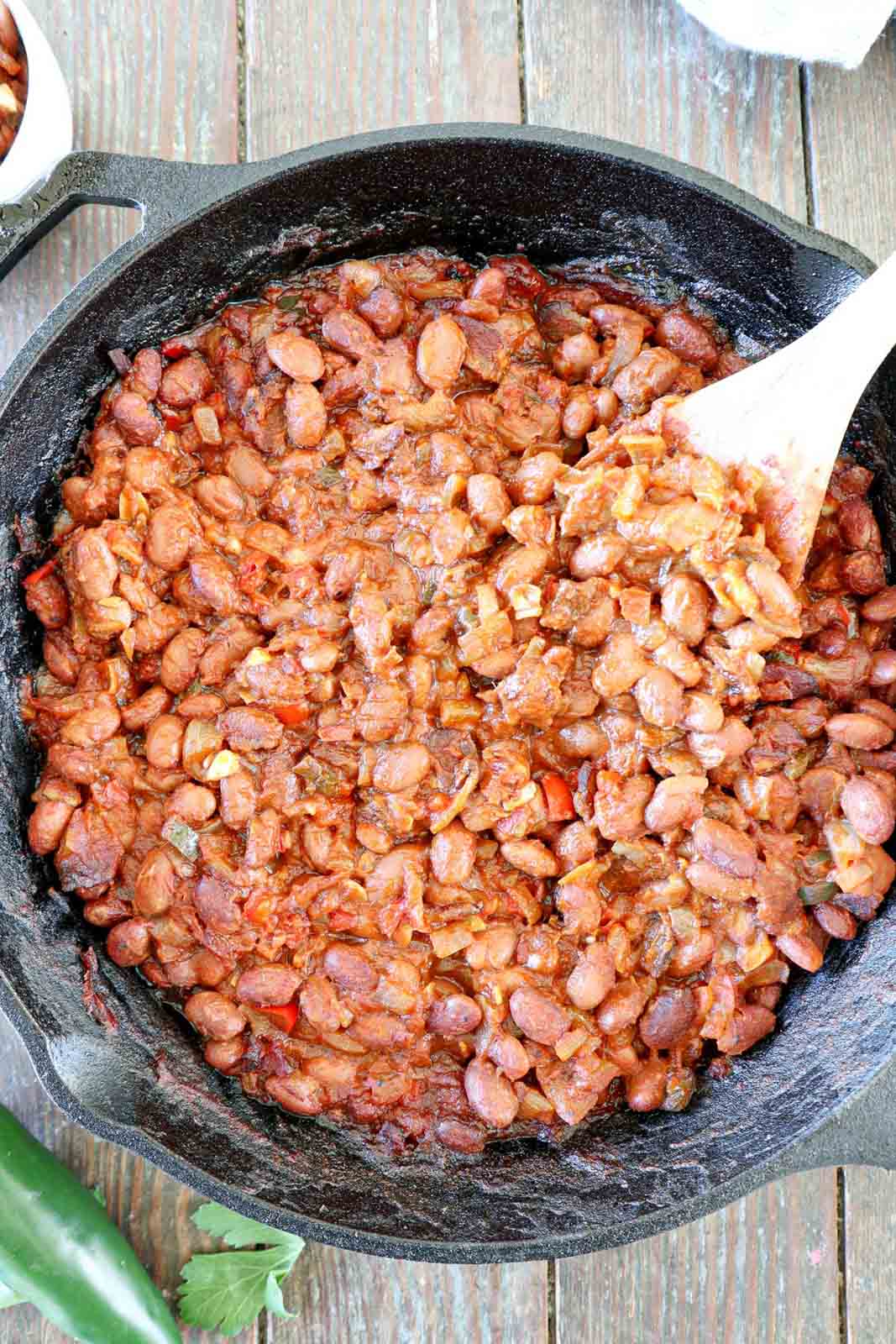 Traeger Baked beans in a cast iron skillet with a wooden spoon.