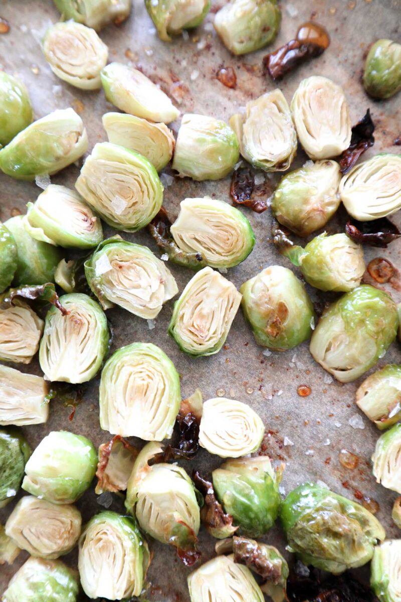 Sliced Brussels sprouts roasted on a baking sheet, showcasing a light golden-brown color, sprinkled with salt. The veggies are arranged in a scattered pattern, highlighting their texture and roasted edges.