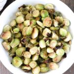 A bowl of roasted Brussels sprouts, halved and slightly browned. The sprouts are arranged in a white dish, showcasing their green and golden-brown hues.