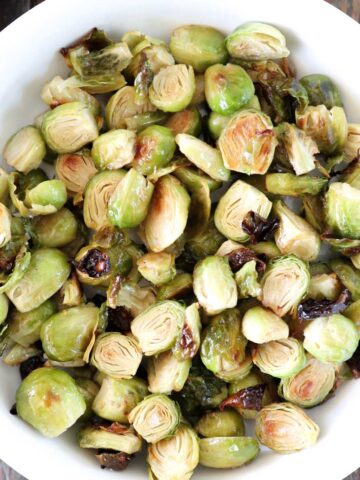 A bowl of roasted Brussels sprouts, halved and slightly browned. The sprouts are arranged in a white dish, showcasing their green and golden-brown hues.
