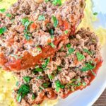 Slices of meatloaf topped with tomato sauce and garnished with chopped parsley are served on a bed of creamy mashed potatoes on a white plate.