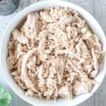 A white bowl filled with shredded chicken pieces on a wooden surface.