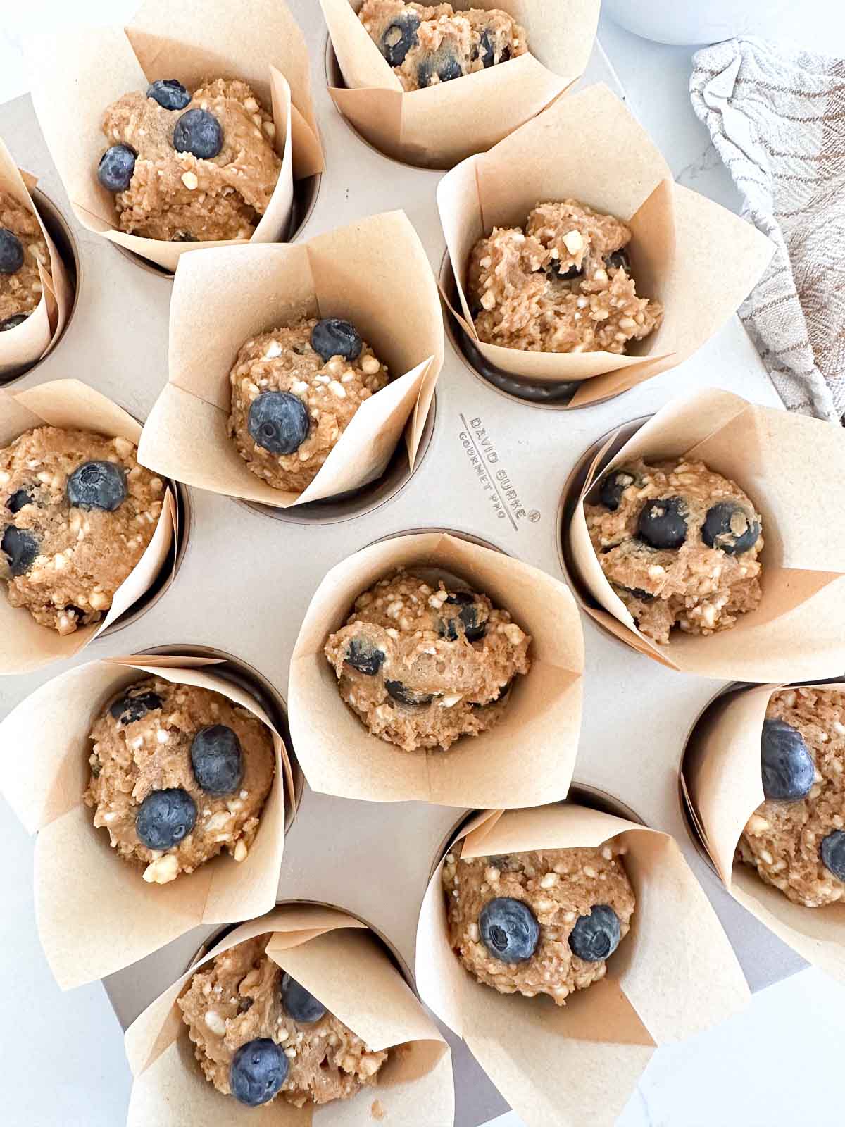 Twelve unbaked blueberry muffins in parchment paper liners arranged on a baking tray.