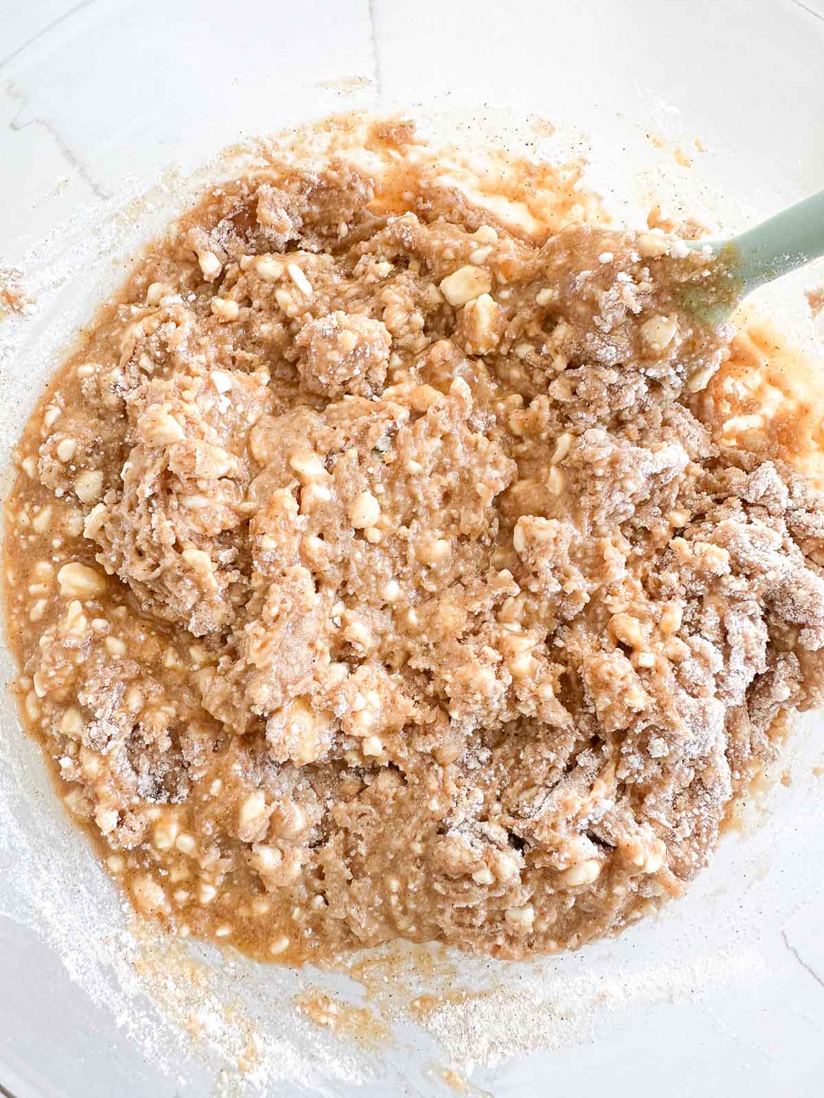 Close-up of a mixing bowl containing blueberry cottage cheese muffin batter. A light green spatula is partially submerged in the mixture.