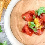 Close-up of a bowl filled with cottage cheese taco dip topped with diced tomatoes, chilies, and cilantro leaves.
