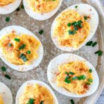 Close-up of gluten free deviled eggs. The eggs are halved, with a creamy yellow filling sprinkled with paprika and garnished with chopped green chives.