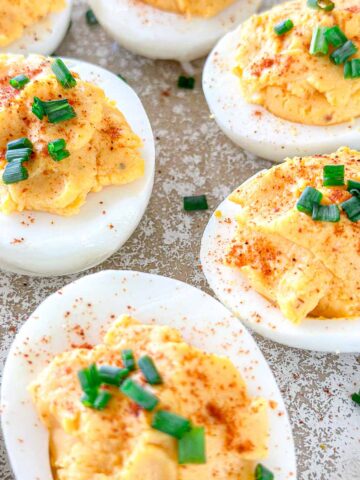 Deviled eggs topped with paprika and chopped green onions arranged on a textured surface.