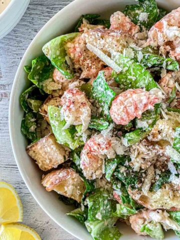 A bowl of Lobster Caesar salad with lettuce, croutons, lobster pieces, and grated cheese, topped with ground pepper.