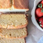 Sliced sourdough pound cake on a parchment paper next to a bowl of fresh strawberries.