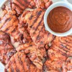 Smoked Boneless Chicken Thighs on a plate with a side of BBQ sauce.