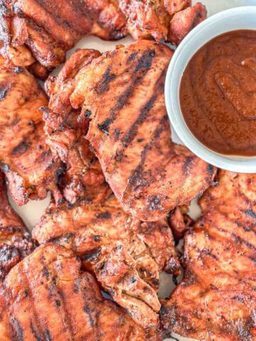Smoked Boneless Chicken Thighs on a plate with a side of BBQ sauce.