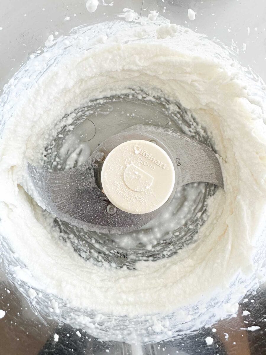A food processor bowl filled with smooth, whipped, cottage cheese. 