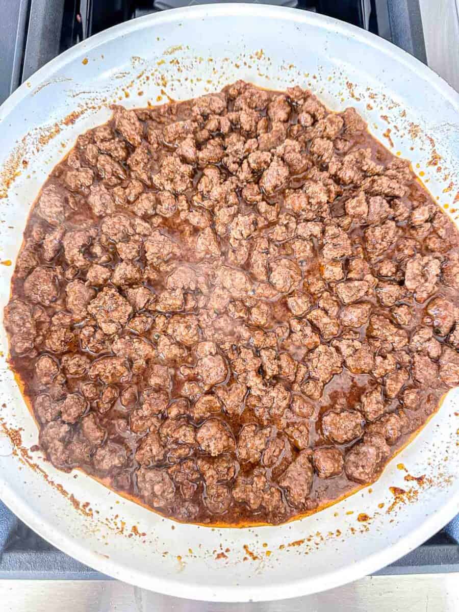 Ground beef cooking in a skillet with taco sauce. 