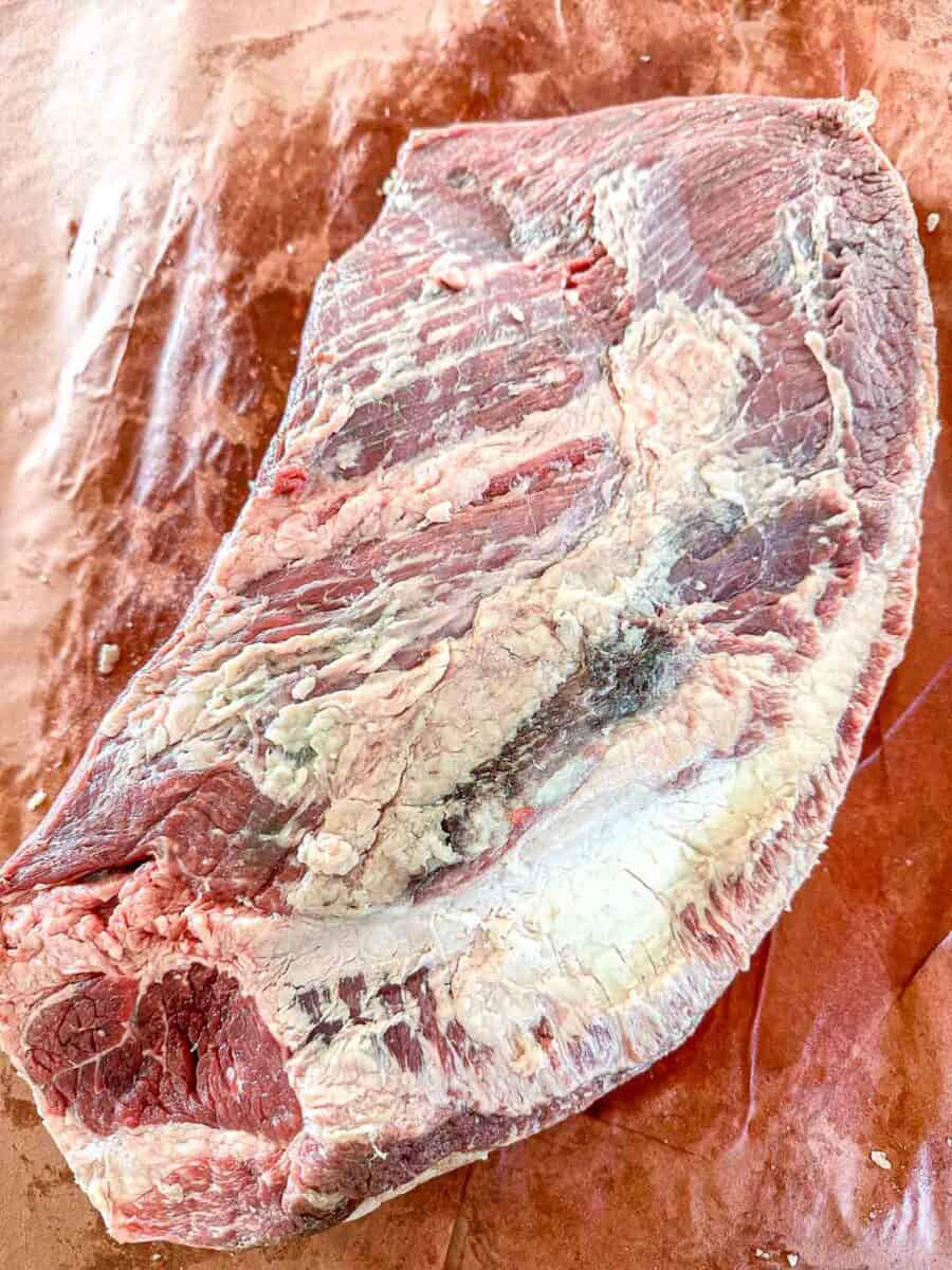 A large, raw cut of brisket with visible marbling and fat sits on brown butcher paper.