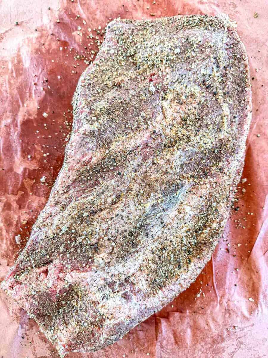 A raw brisket coated with a seasoning blend sits on brown butcher paper.