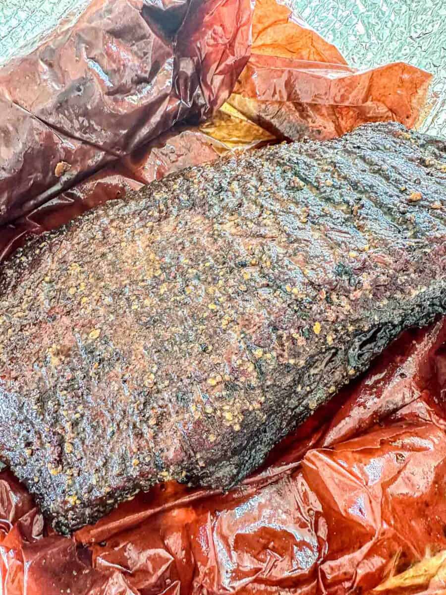 A close-up of a cooked beef brisket with a dark, seasoned crust, resting on reddish-brown butcher paper.