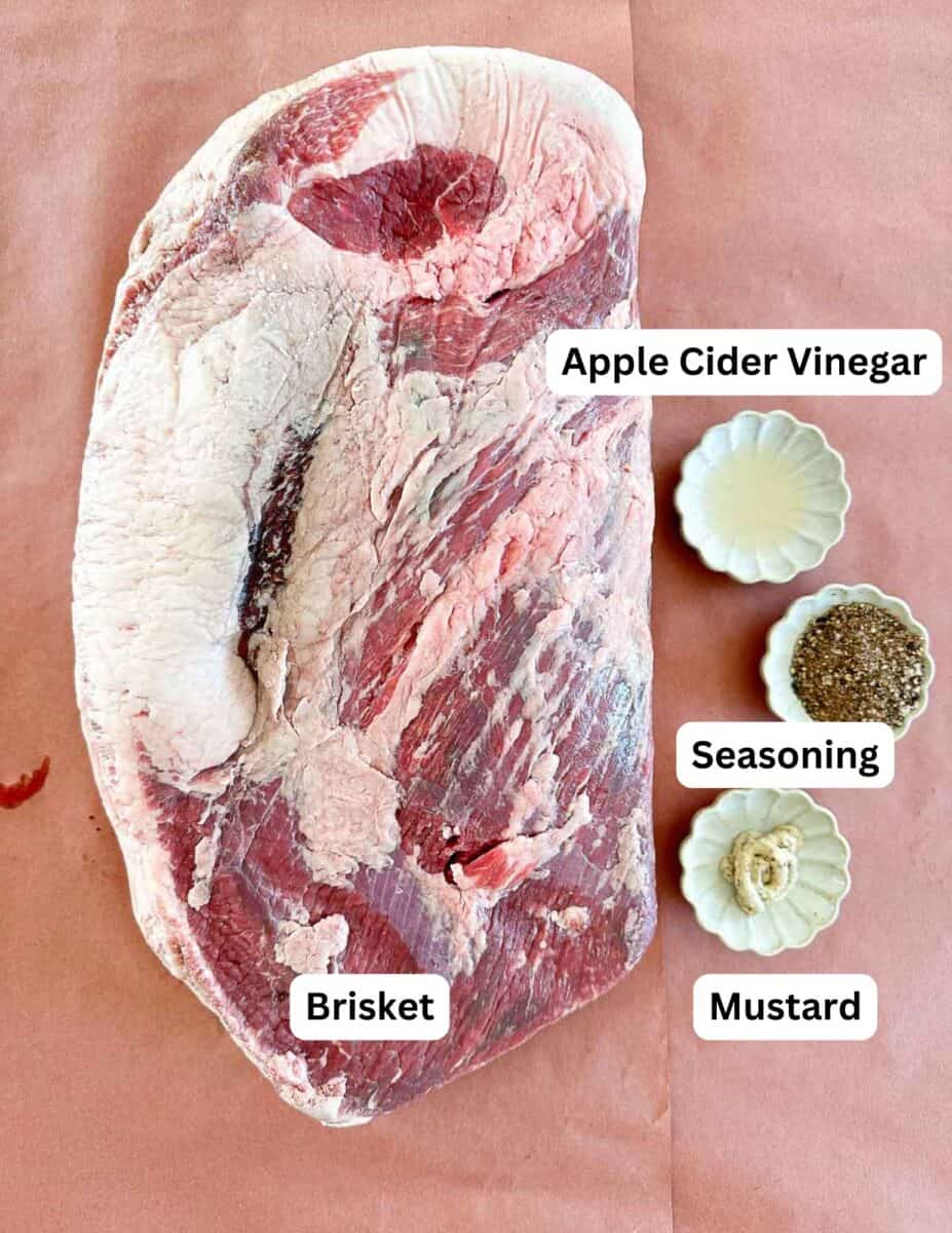Raw brisket on butcher paper next to three small bowls containing apple cider vinegar, a blend of seasonings, and mustard. Each item is labeled with text.
