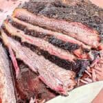 Close-up of sliced smoked brisket showing a dark, seasoned crust and juicy, tender interior with visible smoke ring layers on a cutting board.