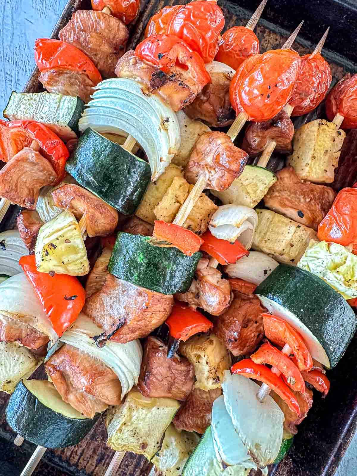 Traeger kabob skewers loaded with grilled chicken, zucchini slices, onion, red bell peppers, tomatoes, and chunks of tofu, all arranged closely together on a tray.