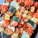 Traeger kabobs of chicken, zucchini, onion, red bell pepper, and pineapple chunks arranged closely together on a dark surface.