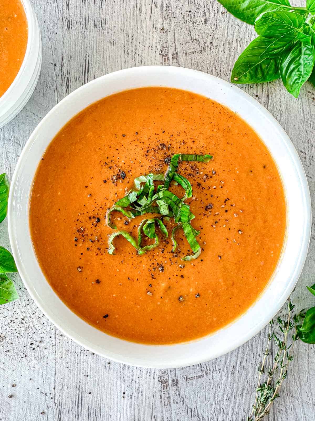 Butternut squash and tomato soup in a white bowl. It's topped with fresh basil and pepper.