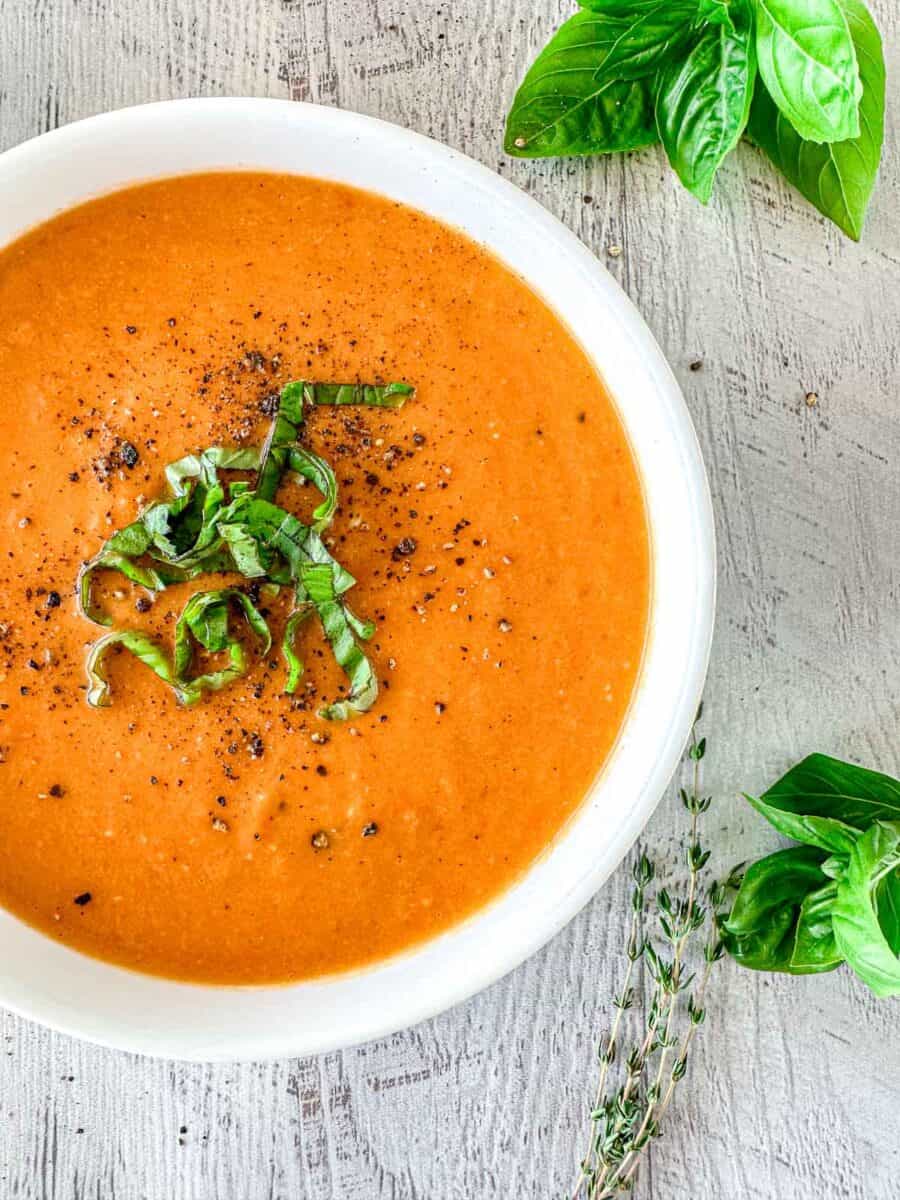 Butternut squash and tomato soup in a white bowl topped with fresh basil and pepper.