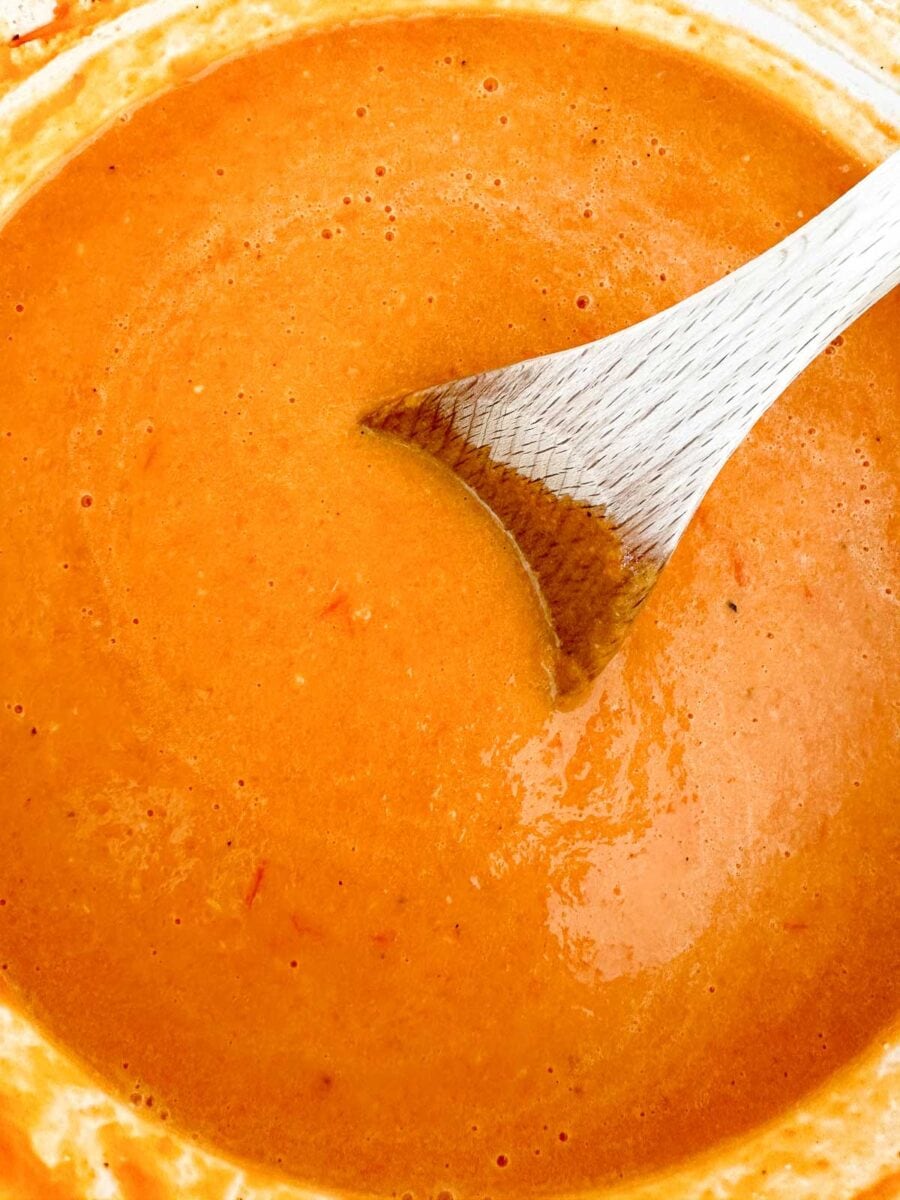 Tomato and butternut squash soup with a wooden spoon.