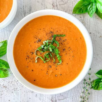 Butternut Squash And Tomato Soup in a white bowl topped with fresh herbs and black pepper.