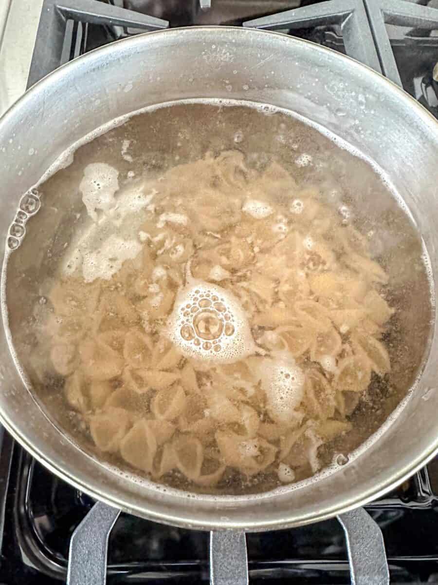 A pot of pasta shells boiling in water on a stovetop, with bubbles and foam forming on the surface.