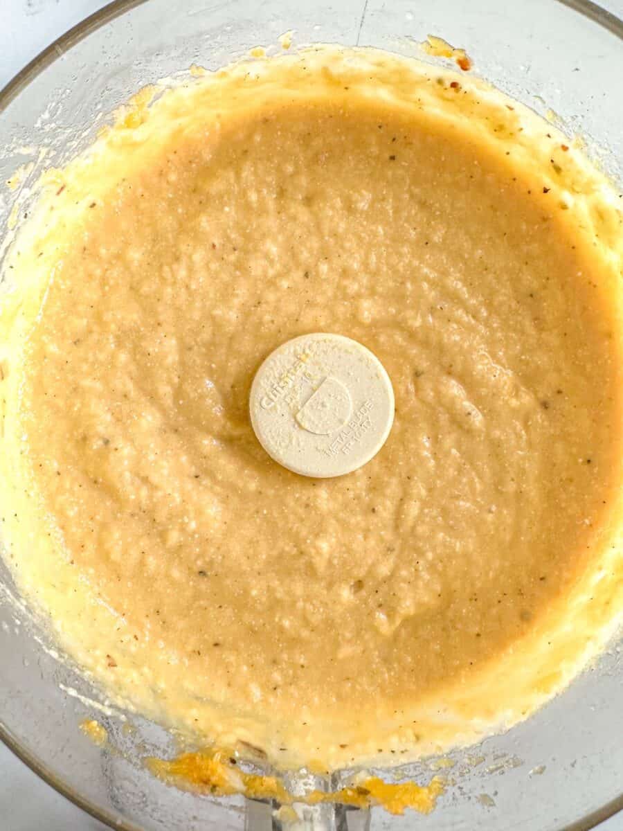 A close-up of a food processor bowl with blended butternut squash and feta.