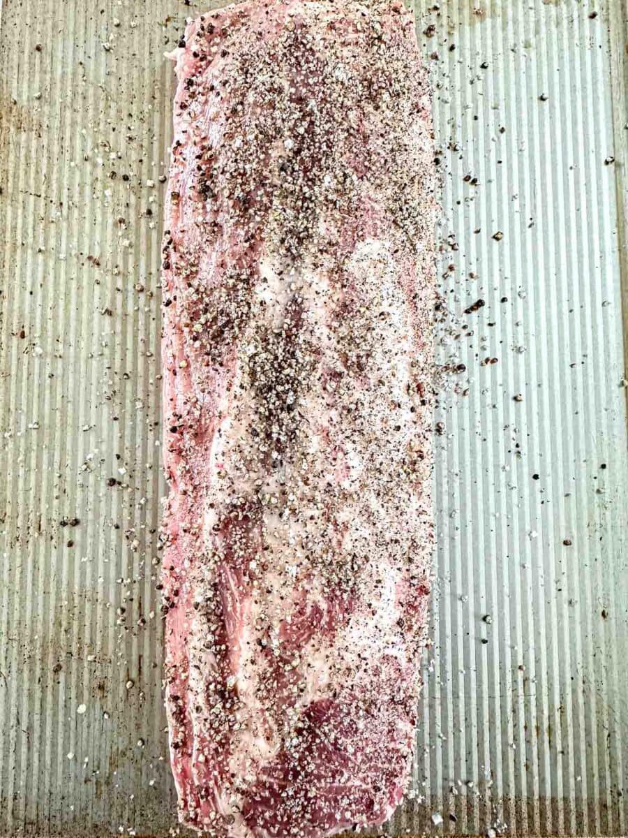 Meaty side of baby back ribs seasoned with salt and pepper.
