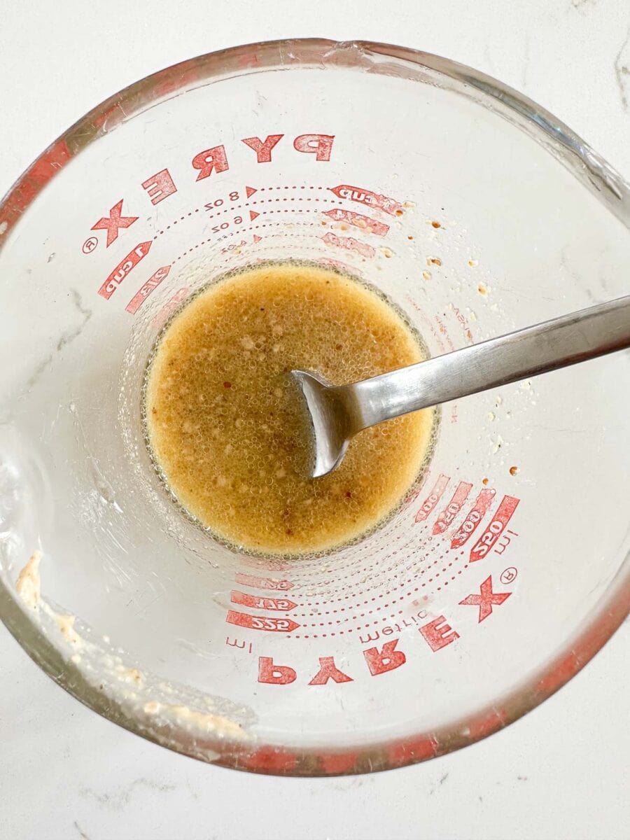 A maple dijon dressing in a glass measuring up with a fork.