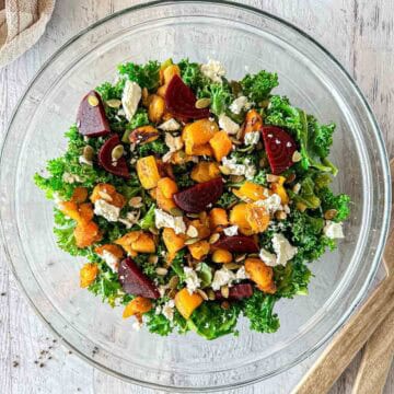 A glass bowl filled with butternut squash feta salad over kale.