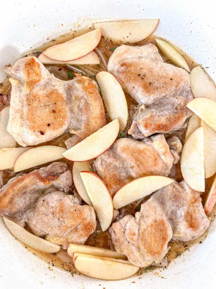Boneless chicken thighs in a dutch oven with sliced apples and braising liquid.