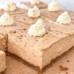 Slices of no-bake pumpkin cheesecake bars with a light brown color, each topped with a swirl of whipped cream and a sprinkle of cinnamon, on a brown parchment-lined surface.