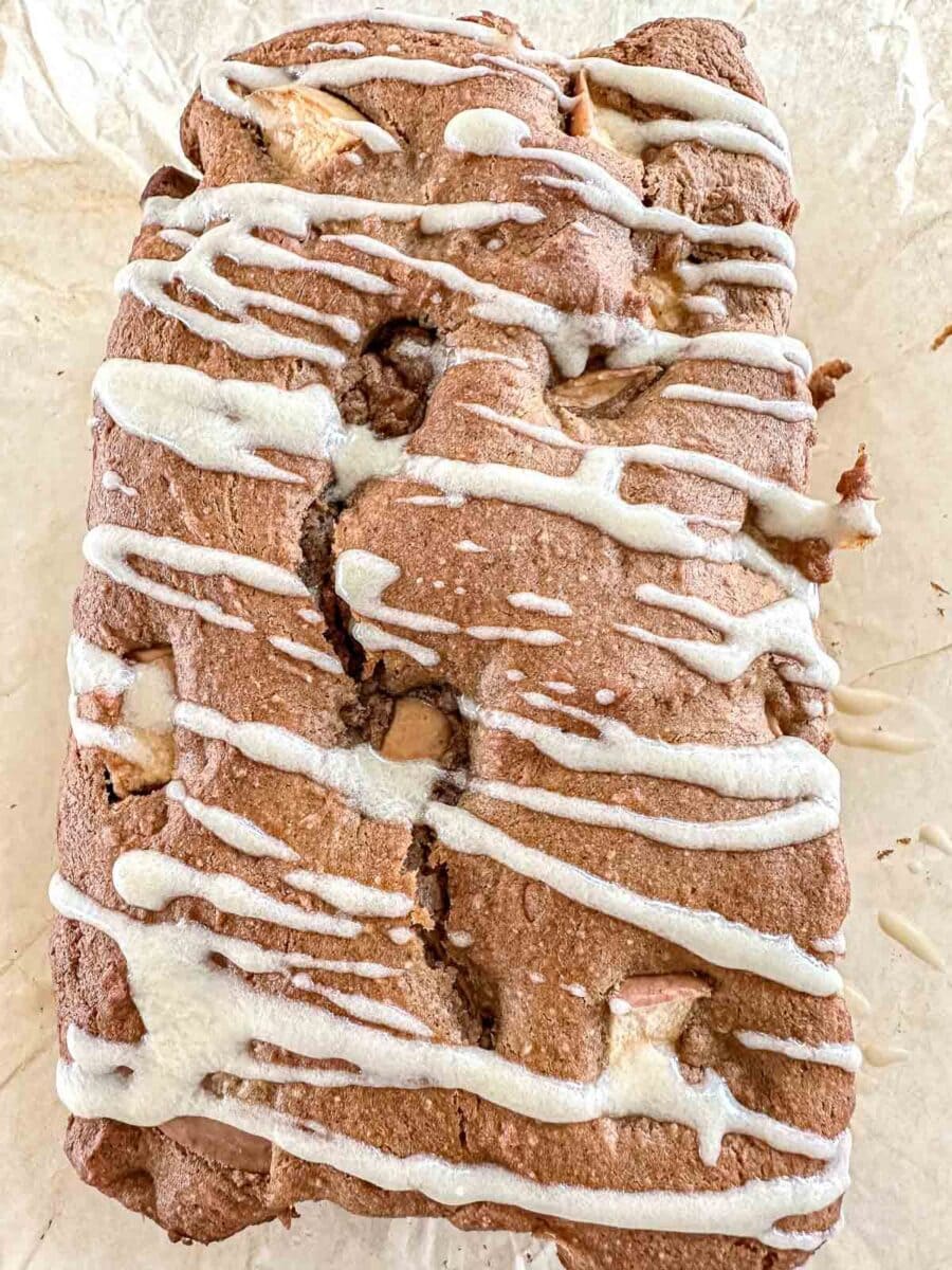 sourdough apple bread on parchment paper. The bread is drizzled with glaze.