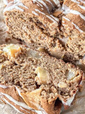Close-up of sliced apple sourdough bread, topped with a light drizzle of icing. The bread is moist, filled with apple chunks, and rests on parchment paper.